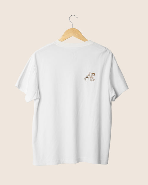 Detalle minimalista en el pecho de la camiseta blanca unisex Before Coffee, mostrando una ilustración lineal marrón de una cafetera moka y una taza humeante.