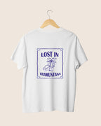 Diseño trasero de la camiseta blanca Lost in Tramuntana de JR.Ilustracions, mostrando un sello rectangular de estilo postal con relieve marino, palmera, cámara retro y tipografía aventurera.