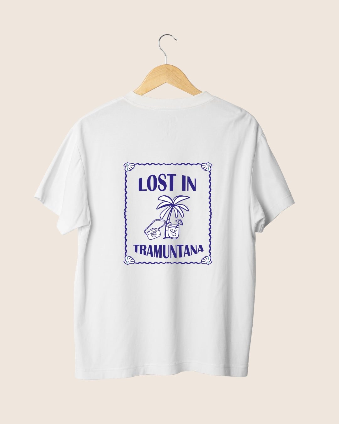 Diseño trasero de la camiseta blanca Lost in Tramuntana de JR.Ilustracions, mostrando un sello rectangular de estilo postal con relieve marino, palmera, cámara retro y tipografía aventurera.