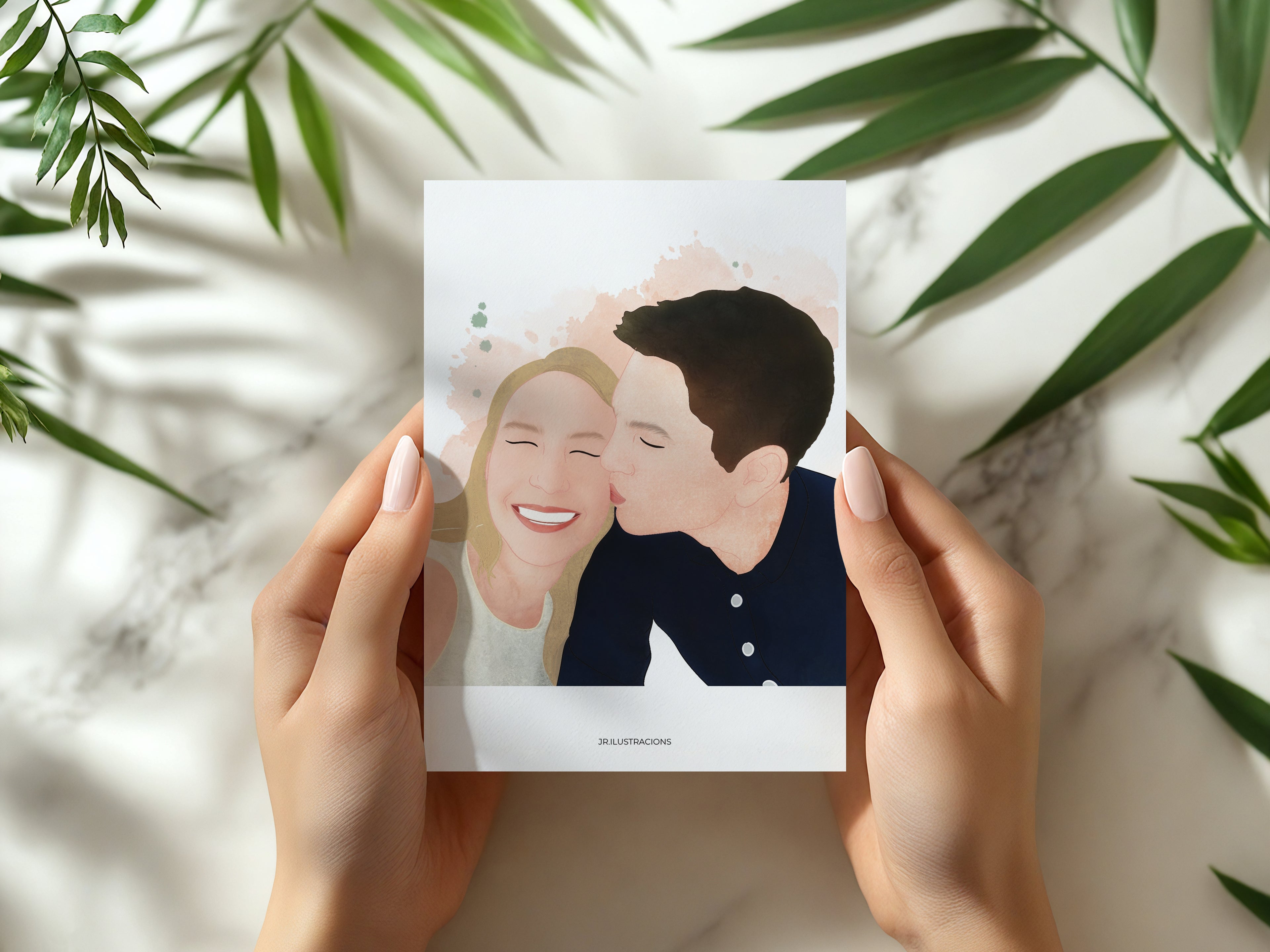 Manos sosteniendo un Mini Recuerdo Ilustrado de 10x15 cm con el retrato de una pareja besándose, sobre fondo de mármol con hojas verdes.